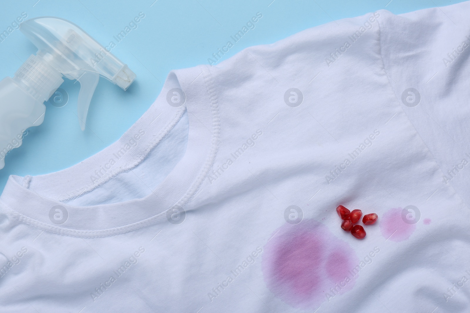 Photo of White shirt with fruit juicy stains, detergent and pomegranate seeds on light blue background, flat lay