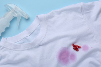 White shirt with fruit juicy stains, detergent and pomegranate seeds on light blue background, flat lay