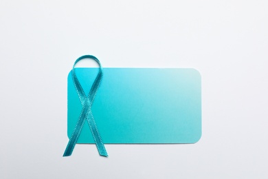 Photo of Teal awareness ribbon and card on white background, top view. Symbol of social and medical issues