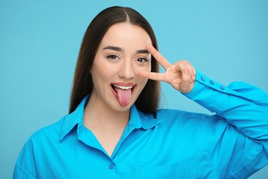 Photo of Happy woman showing her tongue and V-sign on light blue background