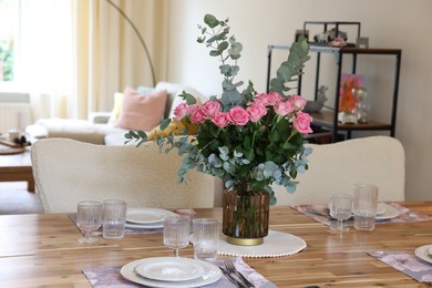 Photo of Beautiful table setting with bouquet in dining room. Roses and eucalyptus branches in vase