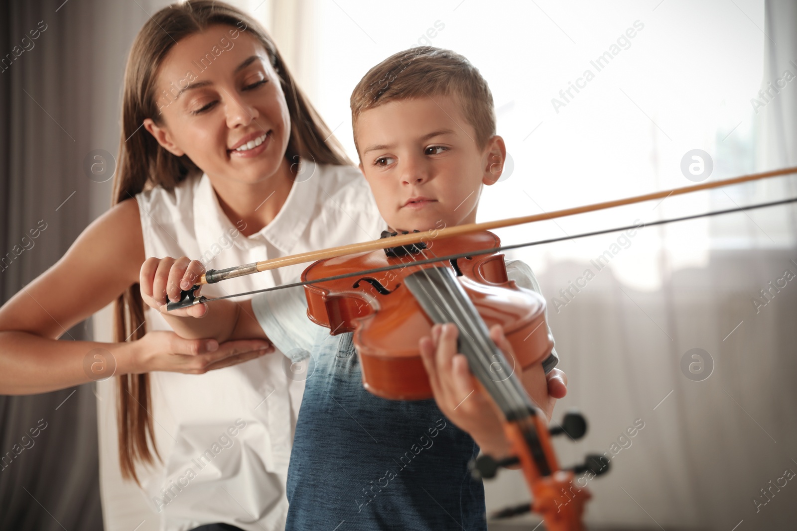 Photo of Young woman teaching little boy to play violin indoors