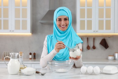 Muslim woman making dough at white table in kitchen