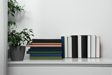 Photo of Many different books and potted plant on white cabinet indoors