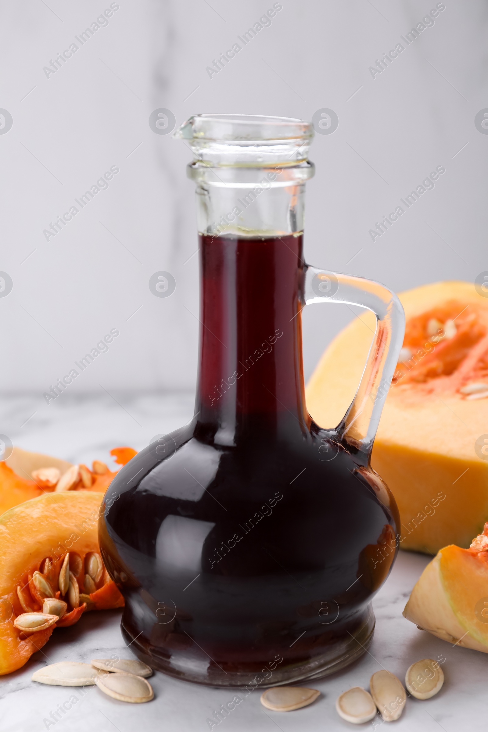 Photo of Fresh pumpkin seed oil in glass jug on white marble table