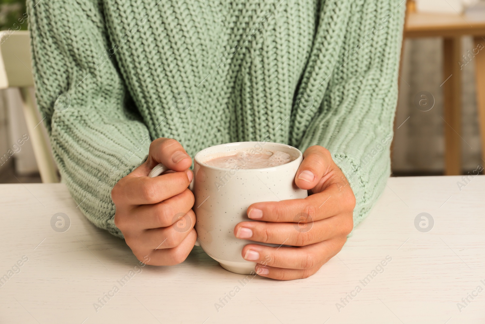 Photo of Woman holding cup of delicious cocoa drink at white table, closeup