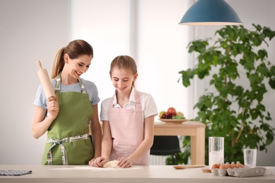 Mother and her daughter preparing dough at table in kitchen