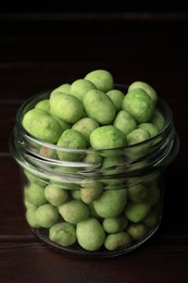 Photo of Tasty wasabi coated peanuts in glass jar on wooden table, closeup