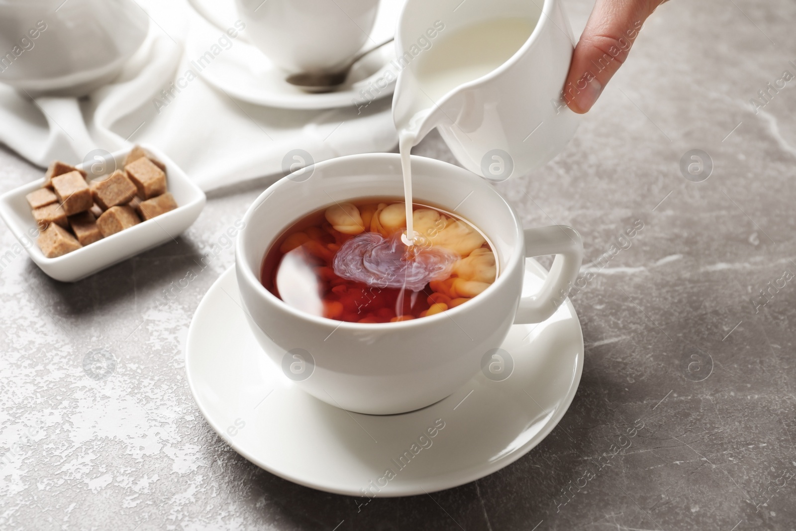 Photo of Pouring milk into cup of black tea on table