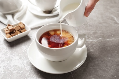 Pouring milk into cup of black tea on table