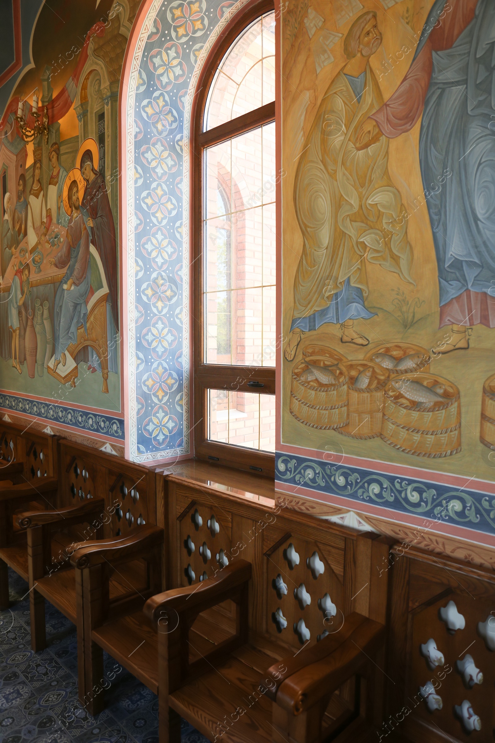 Photo of Empty wooden benches near wall with murals in church