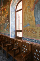 Empty wooden benches near wall with murals in church