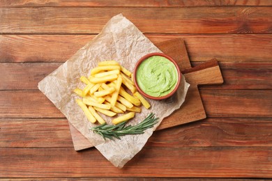 Serving board with parchment, french fries, avocado dip and rosemary on wooden table, top view