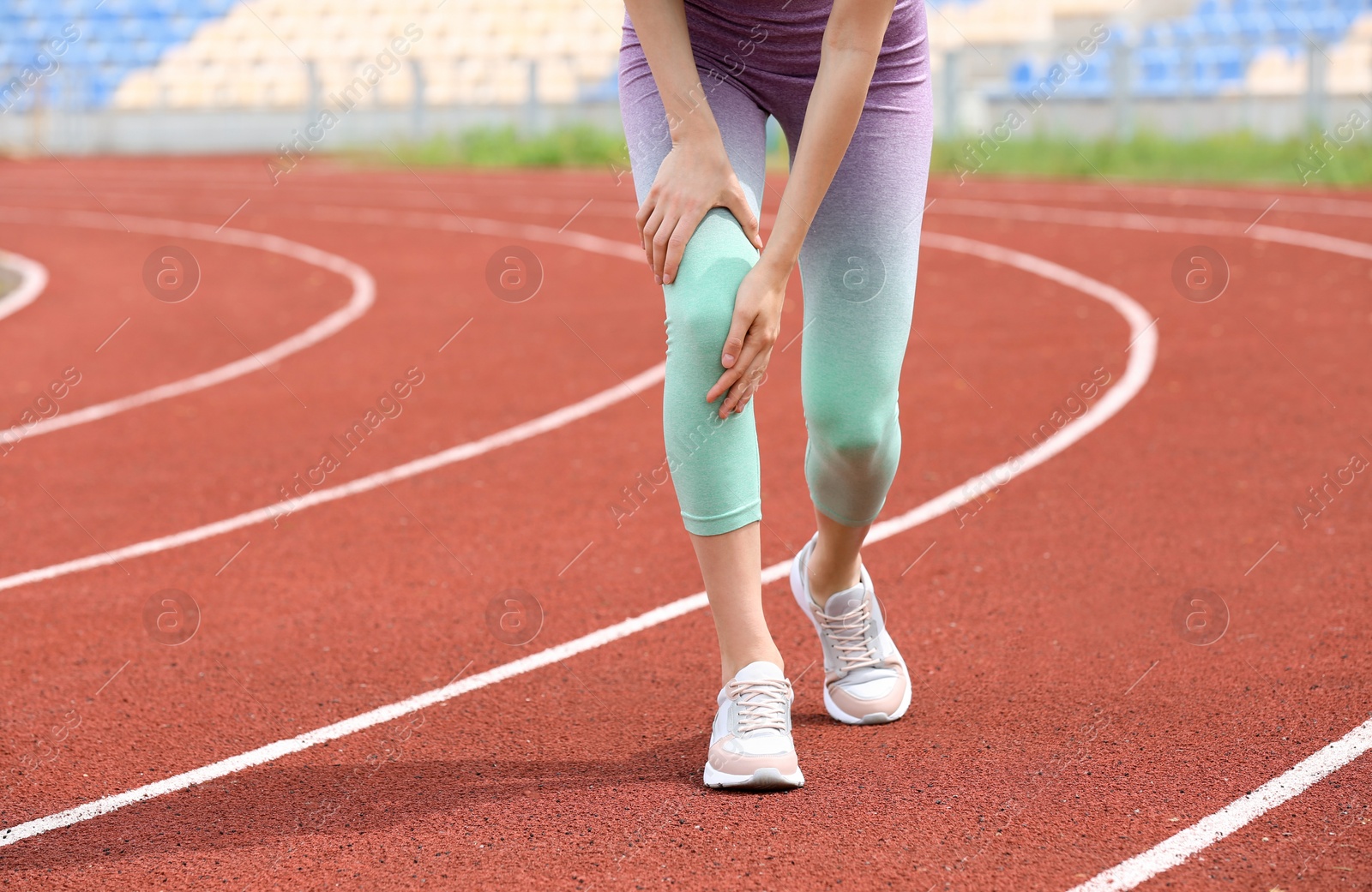 Photo of Woman in sportswear suffering from knee pain at stadium, closeup