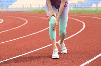 Woman in sportswear suffering from knee pain at stadium, closeup