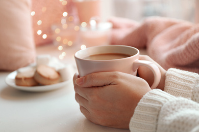 Photo of Woman holding cup of delicious hot coffee at white table, closeup. Winter drink