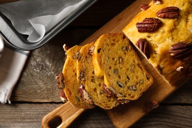 Photo of Cut pumpkin bread with pecan nuts on wooden table, flat lay