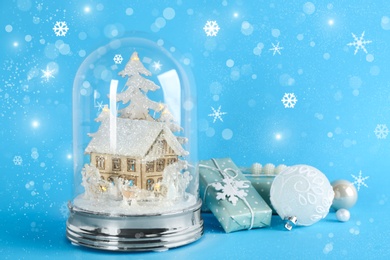 Image of Beautiful Christmas snow globe, gift box and ornaments on light blue background, bokeh effect. Space for text