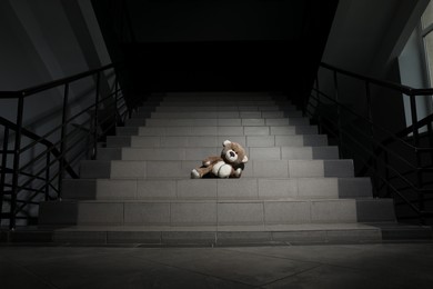 Photo of Lonely teddy bear on grey stairs indoors