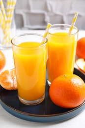 Glasses of fresh tangerine juice and fruits on white table