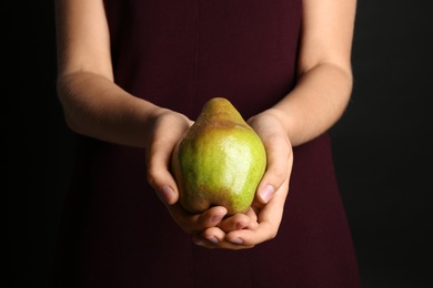 Photo of Woman holding ripe pear on black background, closeup