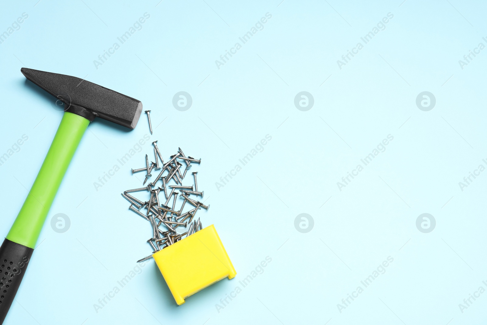 Photo of Hammer and metal nails on light blue background, flat lay. Space for text