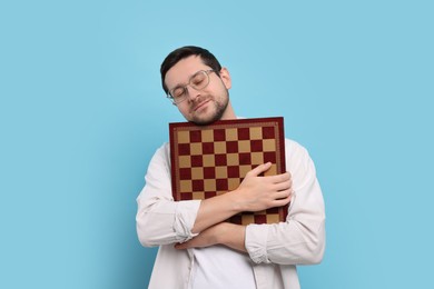 Handsome man holding chessboard on light blue background