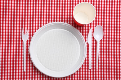 Photo of Table setting with plastic dishware on plaid fabric, flat lay