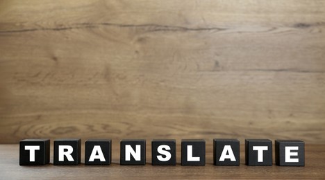 Photo of Word Translate made of black cubes with letters on wooden table. Space for text