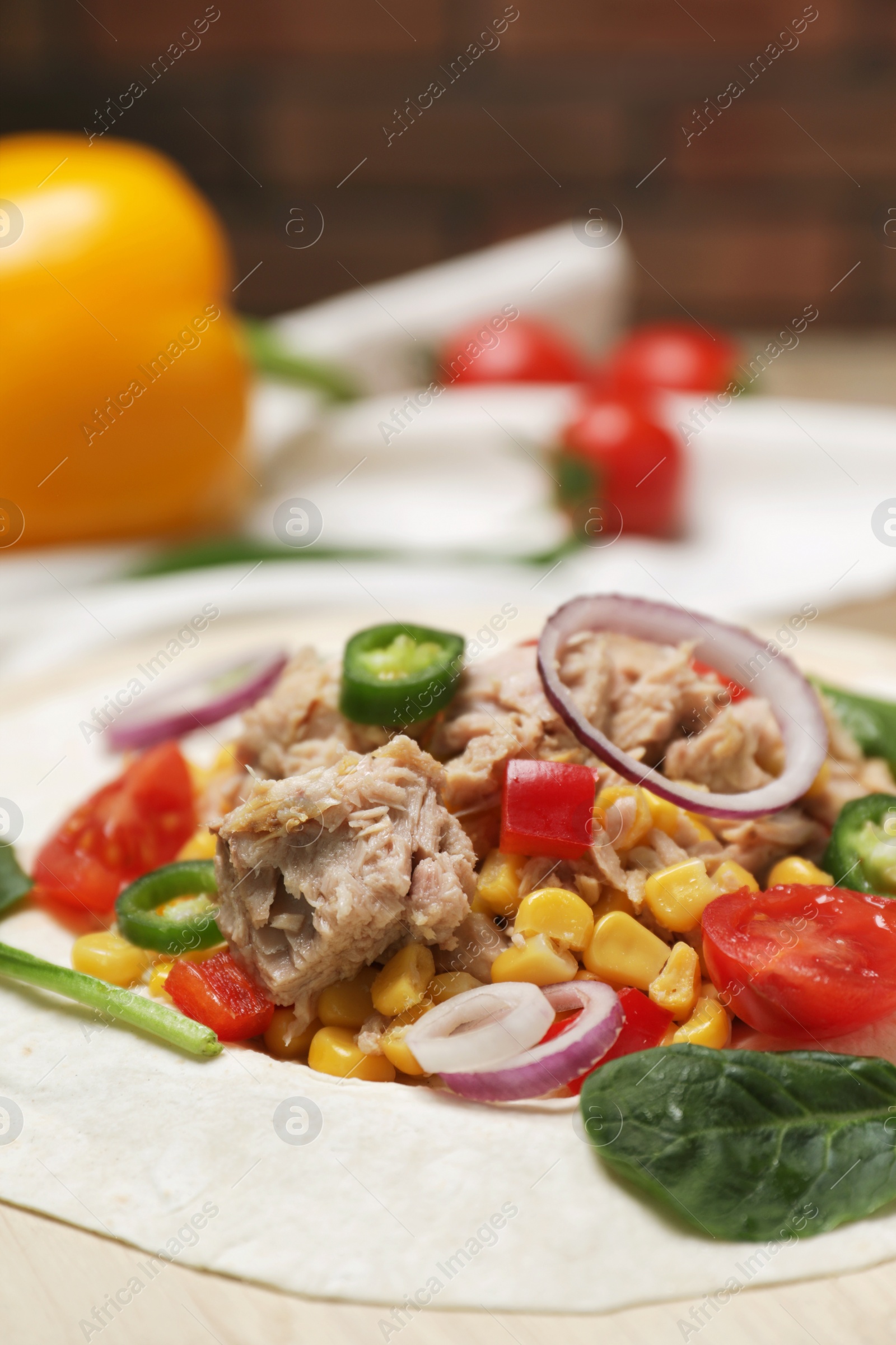 Photo of Delicious tortilla with tuna and vegetables on wooden board, closeup. Cooking shawarma