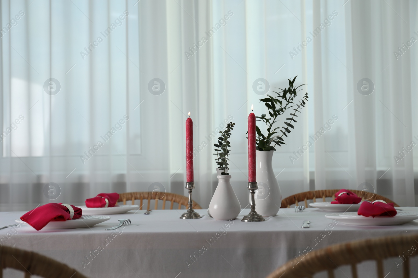 Photo of Beautiful table setting with green branches in vases and burning candles indoors. Stylish dining room