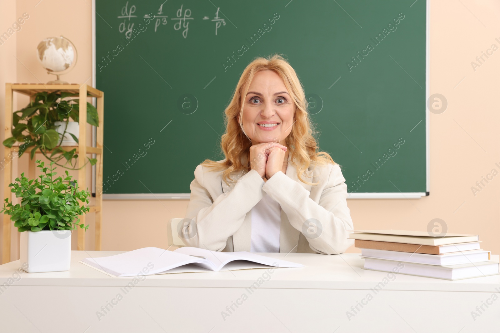 Photo of Happy professor with books sitting at desk in classroom