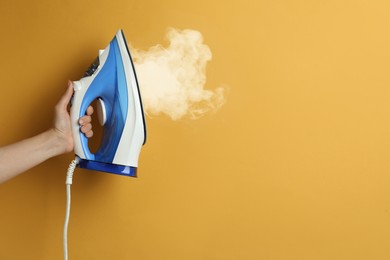 Image of Woman holding modern iron with steam on orange background, closeup. Space for text