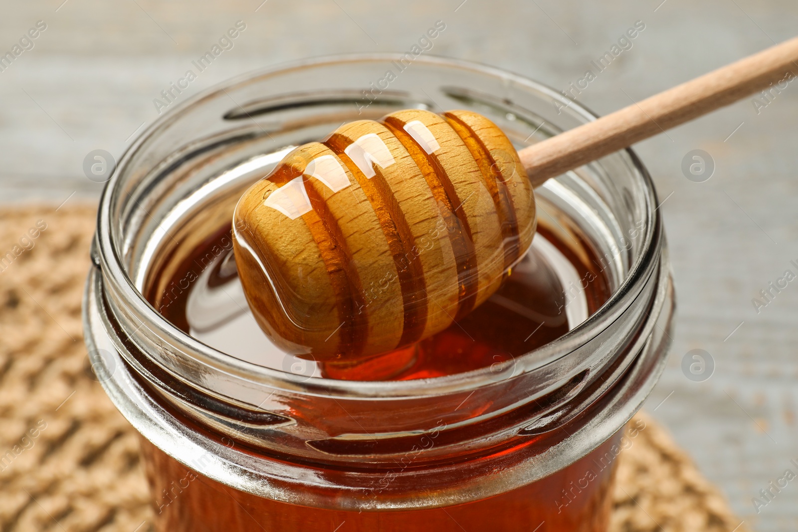 Photo of Glass jar with tasty honey and dipper on grey table, closeup