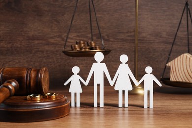 Photo of Divorce concept. Gavel, wedding rings and paper cutout of family on wooden table