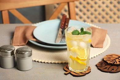 Glass of lemonade and leaf shaped cup coasters on grey wooden table
