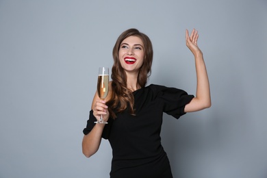 Photo of Happy woman with glass of champagne on grey background. Christmas party