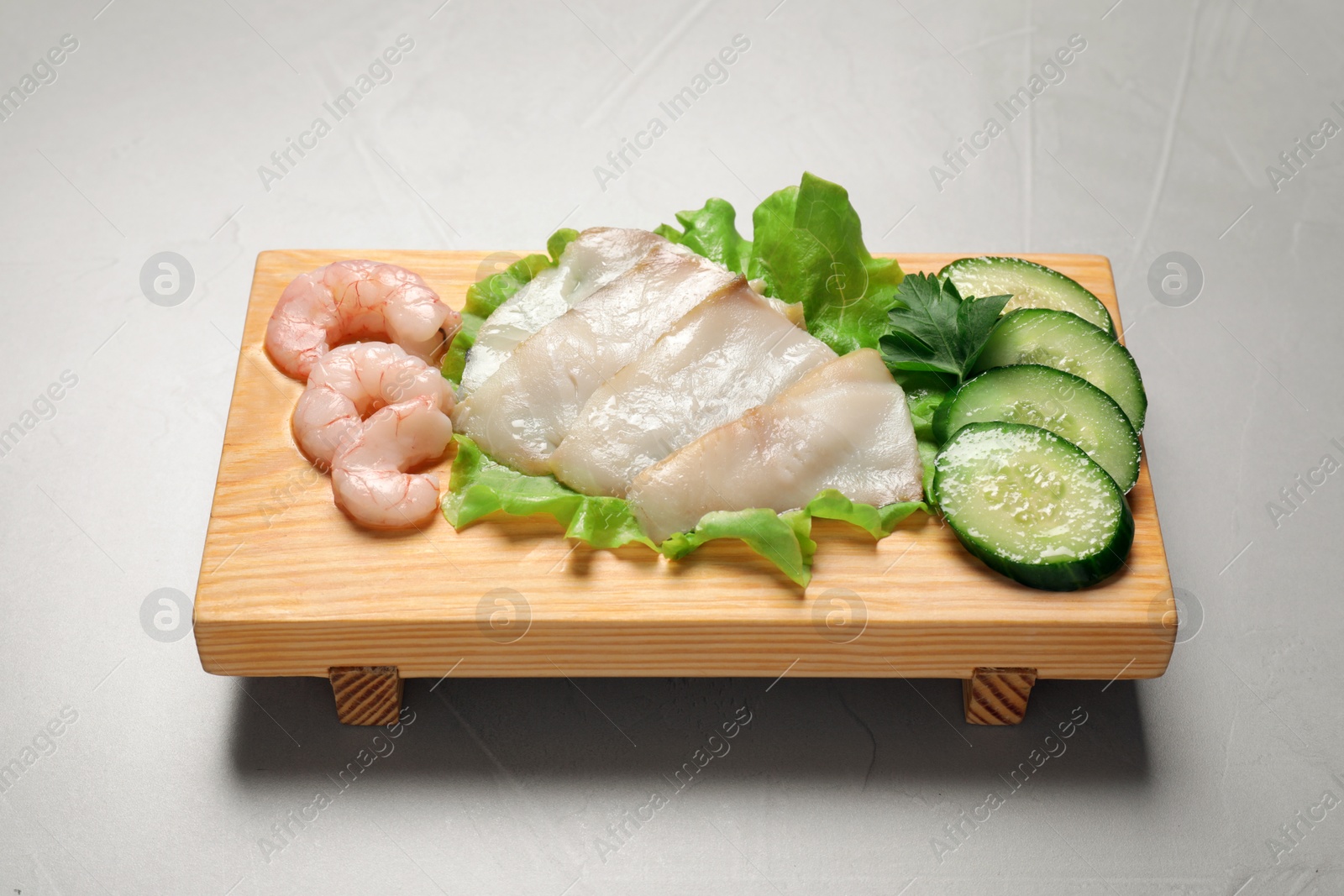 Photo of Sashimi set served with cucumber, lettuce and shrimps on light grey table