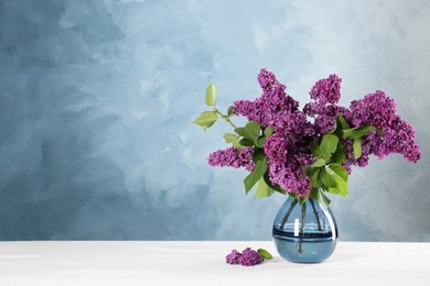 Photo of Beautiful lilac flowers in vase on white table, space for text