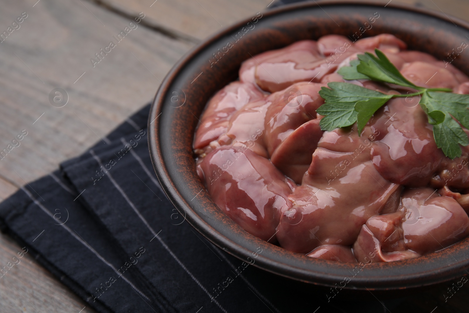 Photo of Bowl with raw chicken liver and parsley on wooden table, closeup. Space for text