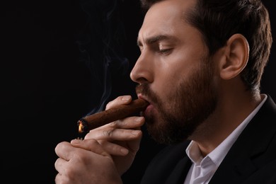 Photo of Handsome man lightning cigar on black background