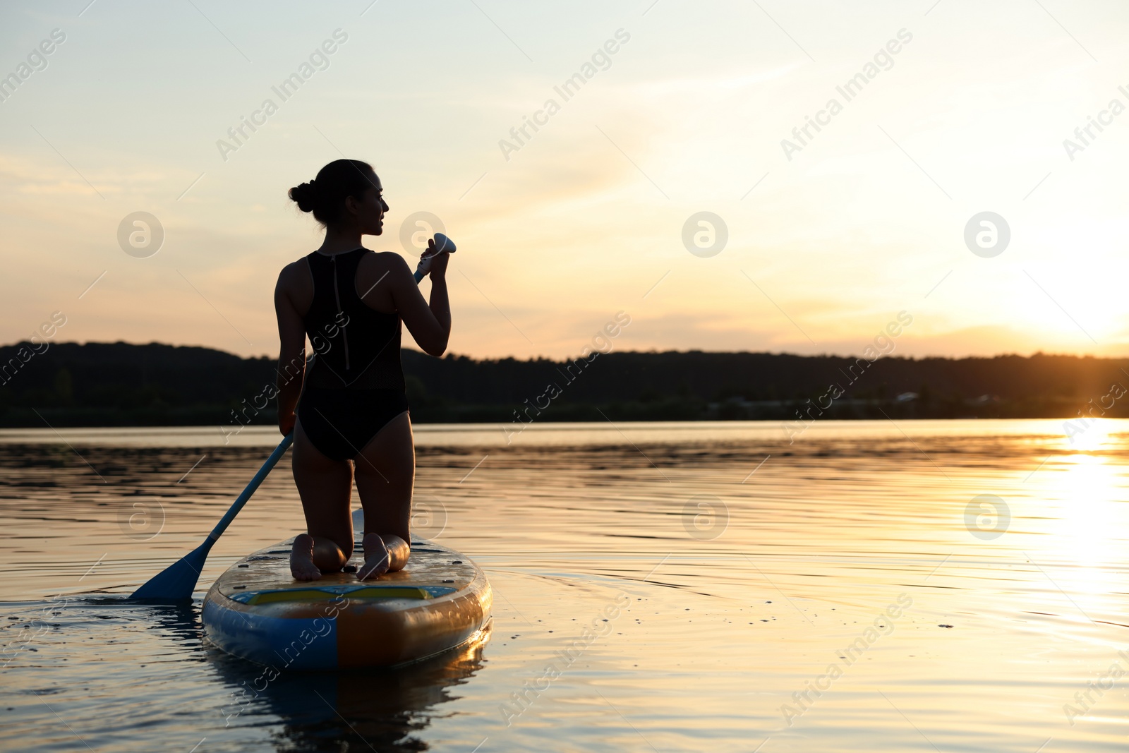 Photo of Woman paddle boarding on SUP board in river at sunset, back view