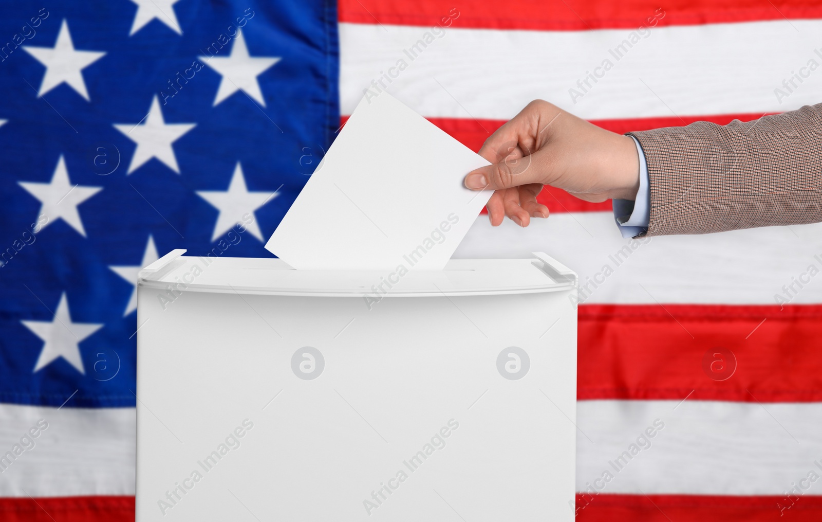 Image of Woman putting her vote into ballot box against national flag of United States, closeup