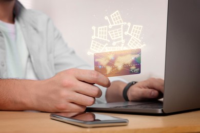 Image of Man using laptop for online purchases at table, closeup. Shopping cart icons flying out of credit card