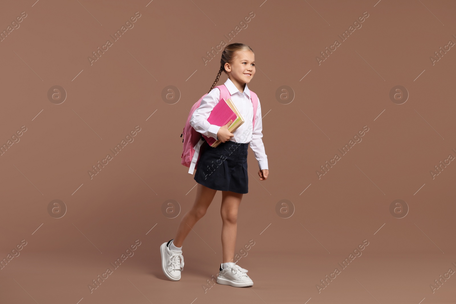 Photo of Happy schoolgirl with backpack and books on brown background