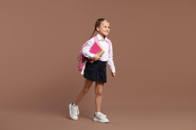 Happy schoolgirl with backpack and books on brown background