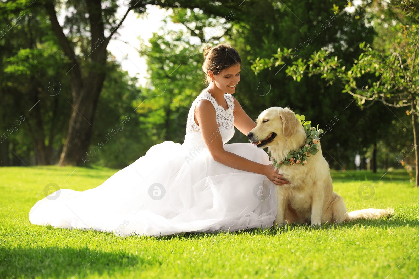 Photo of Bride and adorable Golden Retriever wearing wreath made of beautiful flowers on green grass outdoors