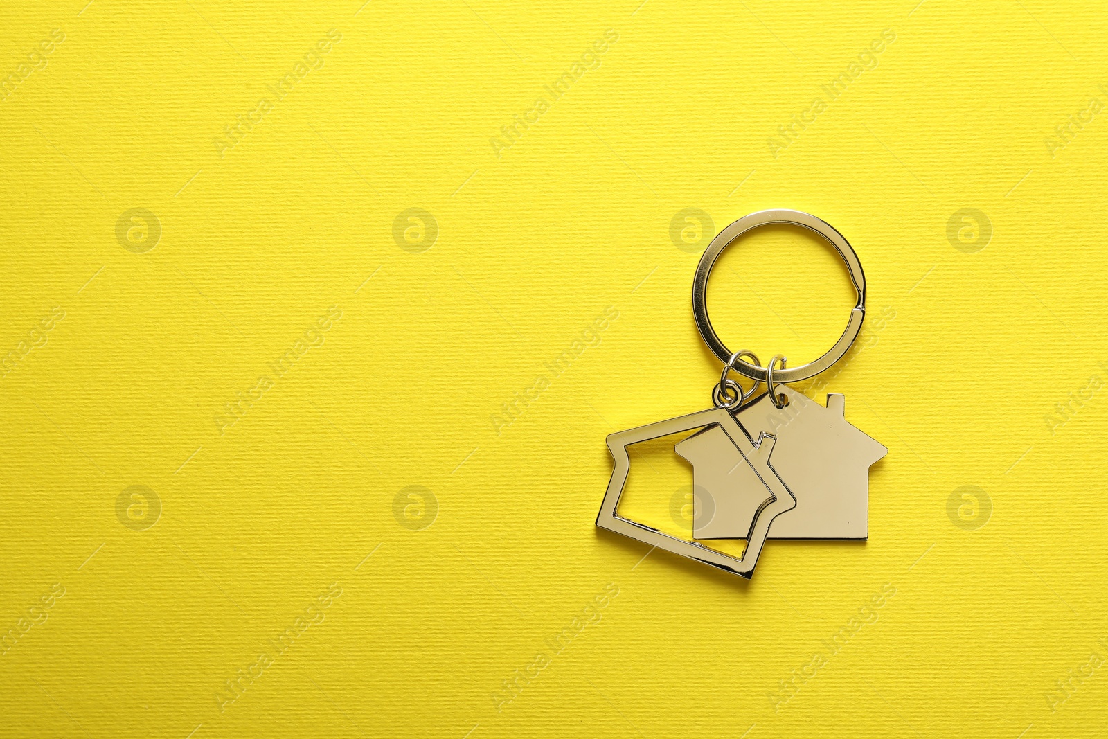Photo of Metallic keychains in shape of houses on yellow background, top view. Space for text