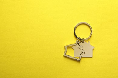 Photo of Metallic keychains in shape of houses on yellow background, top view. Space for text