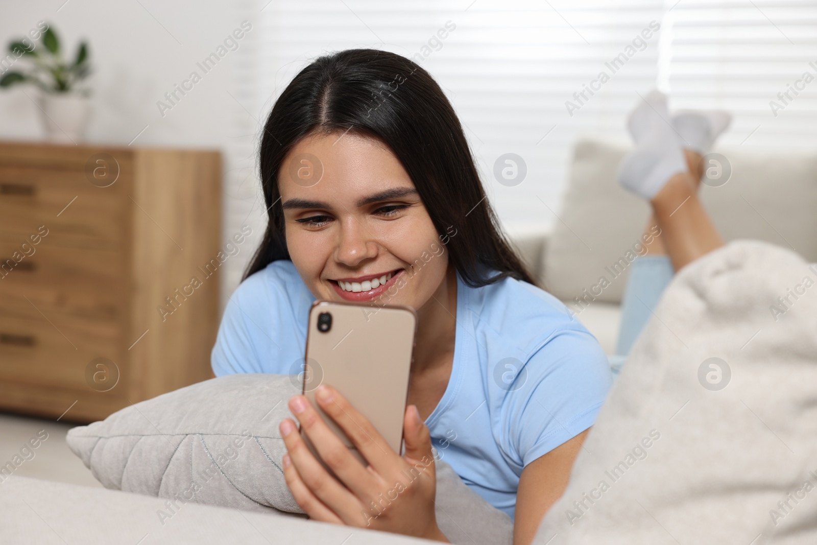 Photo of Happy young woman having video chat via smartphone on sofa in living room